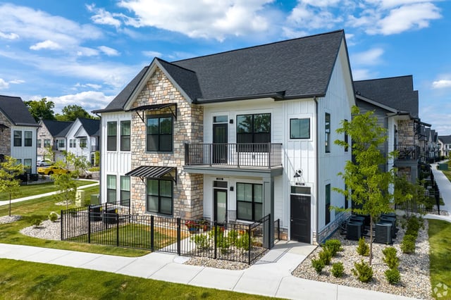 Exterior view of modern townhome apartments with stone and white siding, balconies, and manicured landscaping.