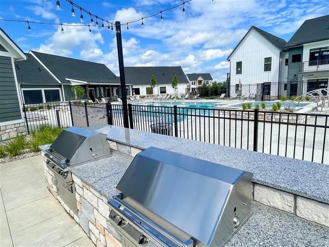 Outdoor grilling station and swimming pool area with lounge chairs and string lights.