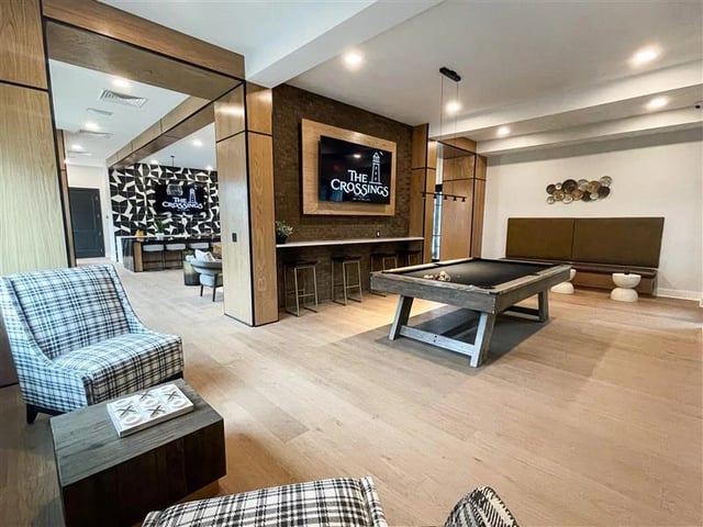 Game room with pool table, seating, and The Crossings logo displayed on a screen.