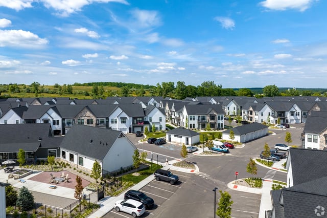 Aerial view of a multifamily property with modern townhomes and manicured landscaping under a bright blue sky.