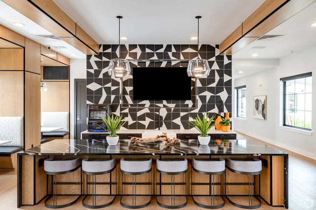 Modern community lounge with a black and white geometric tile backsplash and a large island with bar stools.