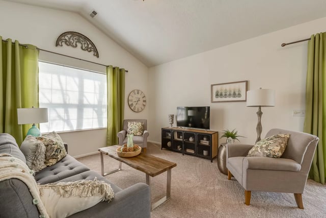 Living room with vaulted ceilings, large window, sofa, armchair, coffee table, and TV.
