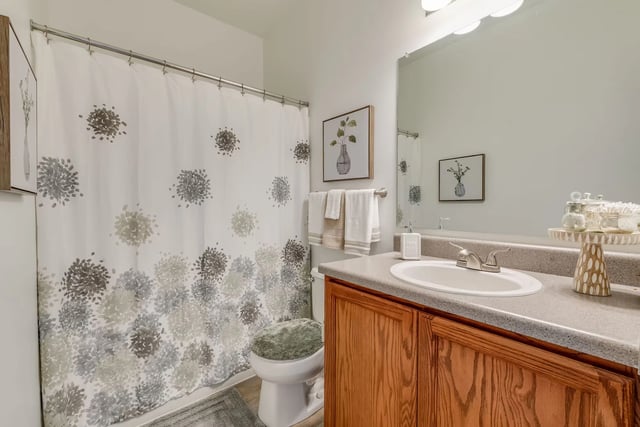 Bathroom with a floral shower curtain and a wooden vanity.