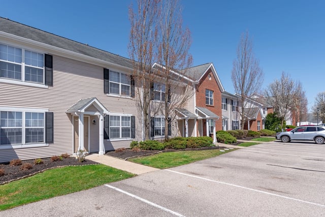 Exterior view of apartment buildings with parking lot and green lawn.