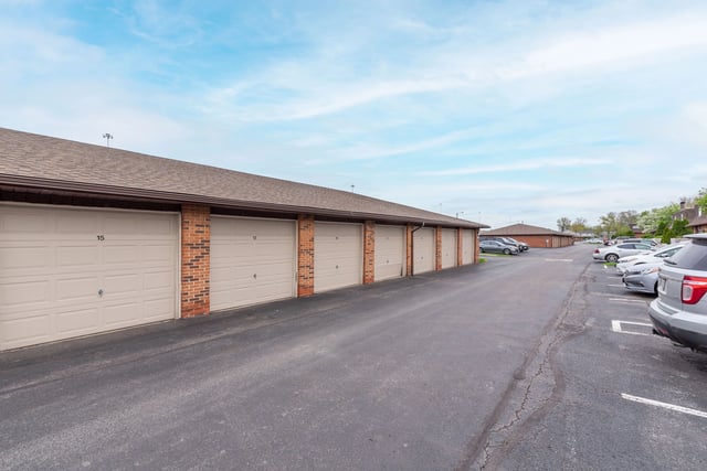 Exterior view of a row of garage doors numbered 15, 17, and others, with a parking lot and cars to the right.