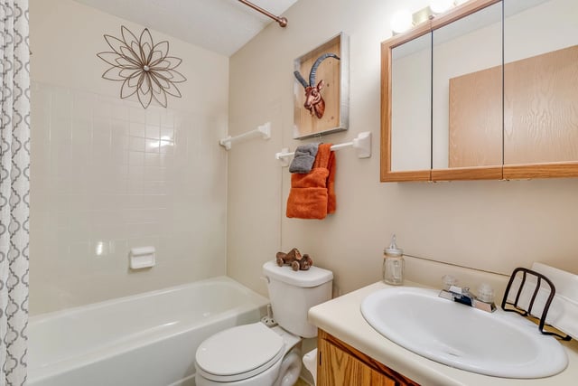 Bathroom with white bathtub, toilet, sink, and mirrored cabinet.