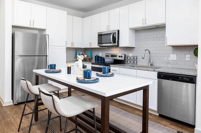 Modern kitchen with white cabinets, stainless steel appliances, and a marble-topped island with seating.