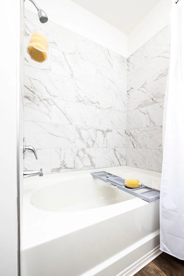 Clean bathroom with a white bathtub, marble tile shower surround, and a hanging bath sponge.