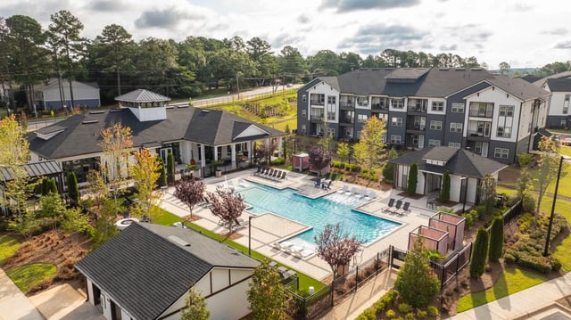 Aerial view of a modern apartment complex featuring a large swimming pool and lounge area.