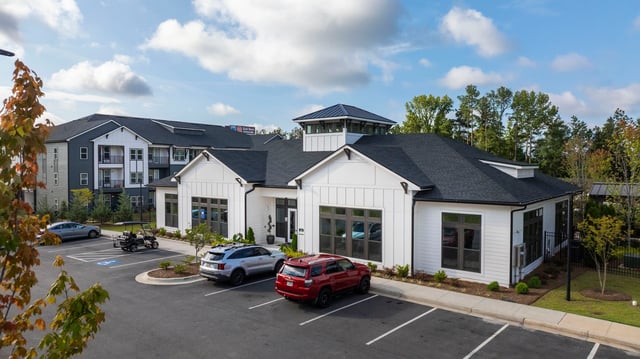 Modern apartment complex with a white clubhouse and a large apartment building in the background.