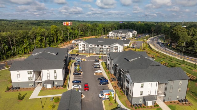 Aerial view of apartment buildings with parking lots and surrounding trees.