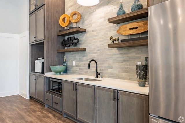 Modern kitchen with gray cabinets, stainless steel appliances, and decorative shelving.