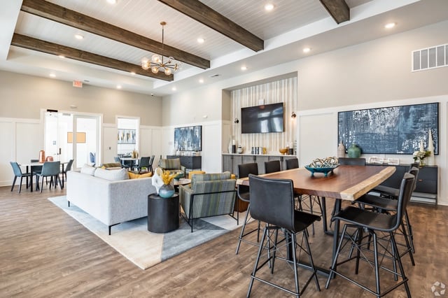 The community lounge area features a large wooden dining table with black chairs, a sectional sofa, and modern decor.
