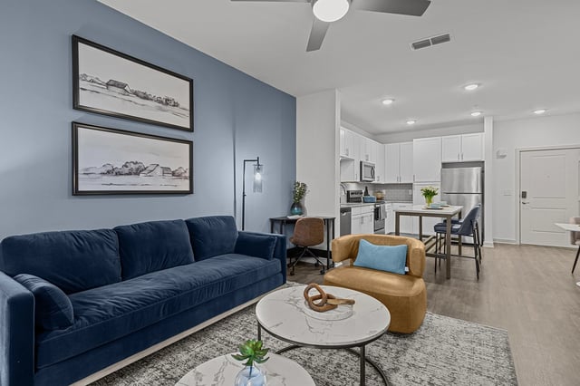 Living room and kitchen area of a modern apartment with blue sofa and white cabinets.
