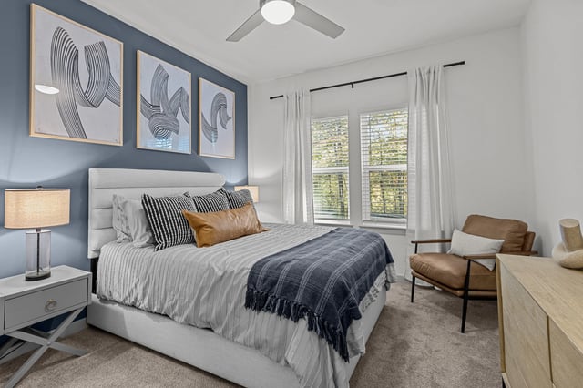 A bedroom with a king-sized bed, modern art, and a leather accent chair.