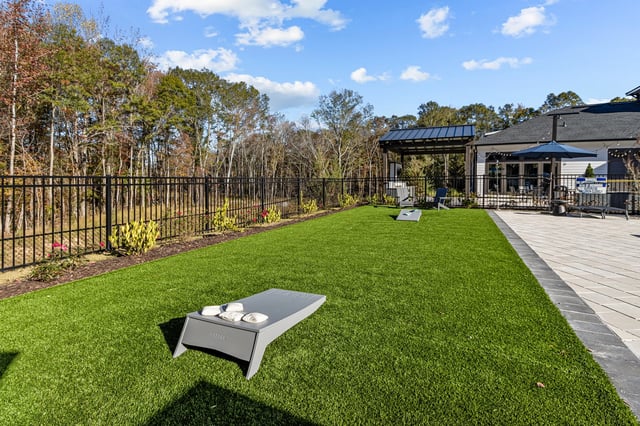 Outdoor lawn area with cornhole game set up, patio furniture under a pergola, and lounge chairs on a paved area.