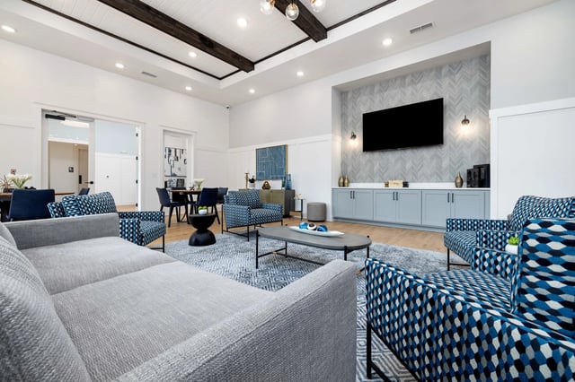 Modern community lounge with comfortable seating, coffee tables, and a large TV.