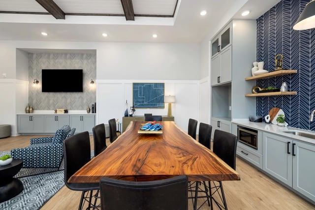 Community lounge with large live-edge dining table, chairs, seating area with TV, and kitchenette.