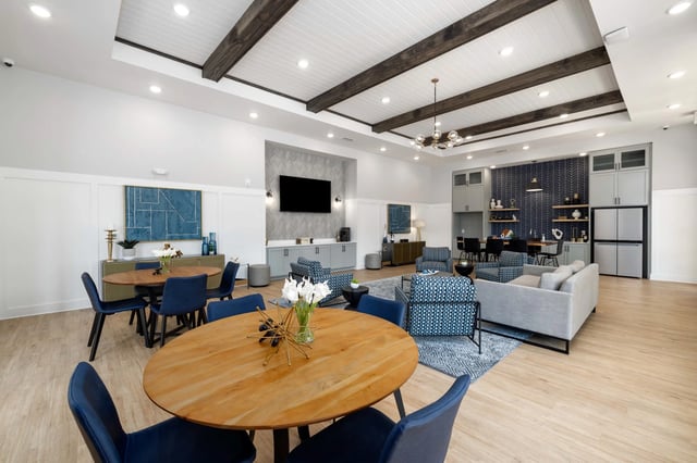 Modern communal lounge area with comfortable seating, dining tables, and a large screen TV.