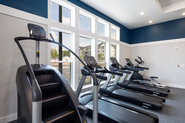 Cardio machines including treadmills and stair climber in a well-lit fitness center.