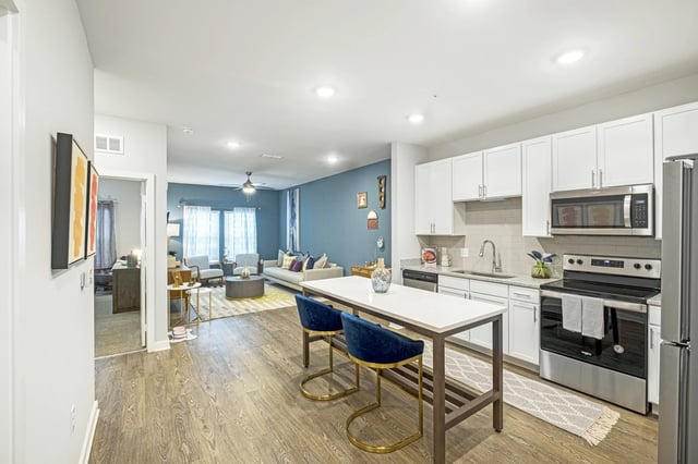 Modern kitchen and living room area with white cabinets, stainless steel appliances, and blue accent wall.