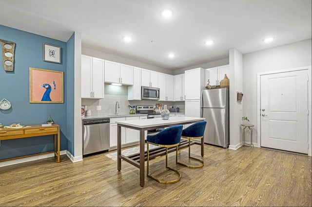 Modern kitchen with white cabinets, stainless steel appliances, and a breakfast island with blue stools.