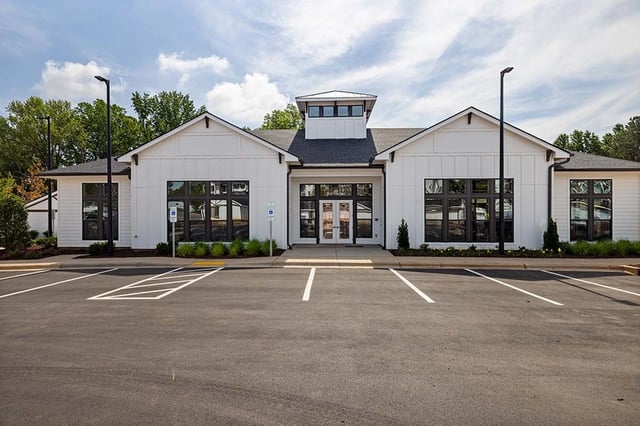 Modern white building with large windows and a parking lot in front.