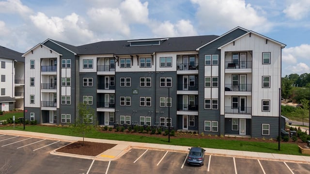 Exterior view of a modern apartment building with multiple balconies and a parking lot.