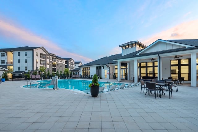 Outdoor swimming pool and lounge area with apartment buildings in the background.