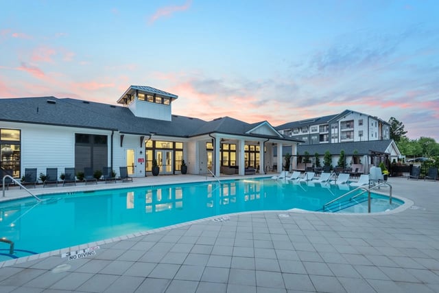 A modern apartment complex with a large swimming pool and lounge chairs at sunset.