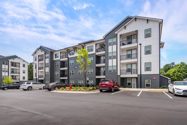 Exterior of a modern apartment building with multiple balconies and a parking lot.