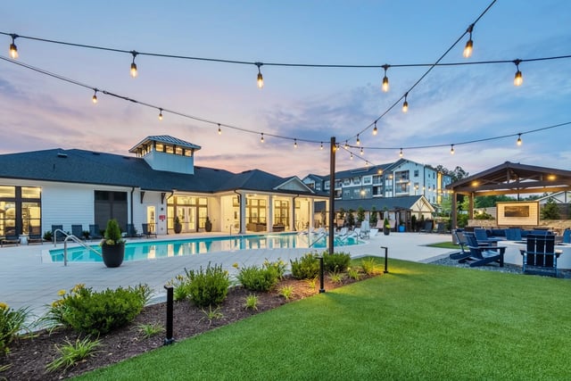 Outdoor swimming pool and lounge area with string lights and fire pit at dusk.