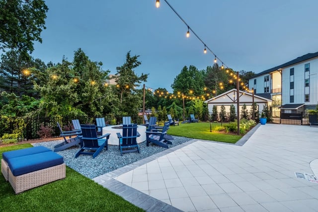 Outdoor communal area with a fire pit, Adirondack chairs, and string lights.