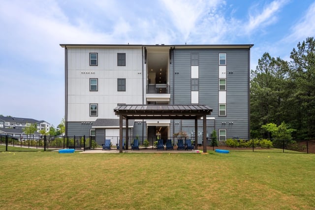 Exterior of a modern apartment building with a covered patio and lawn.