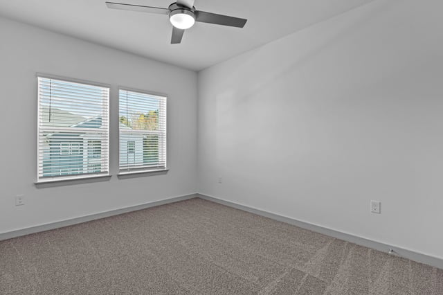Empty bedroom with two windows and a ceiling fan.