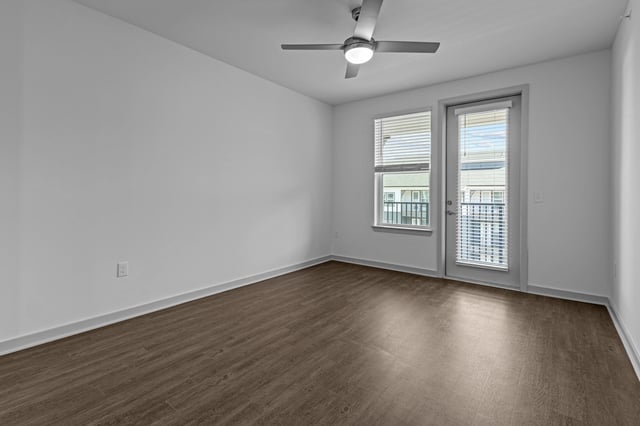 Empty room with hardwood floors, ceiling fan, window, and balcony door.