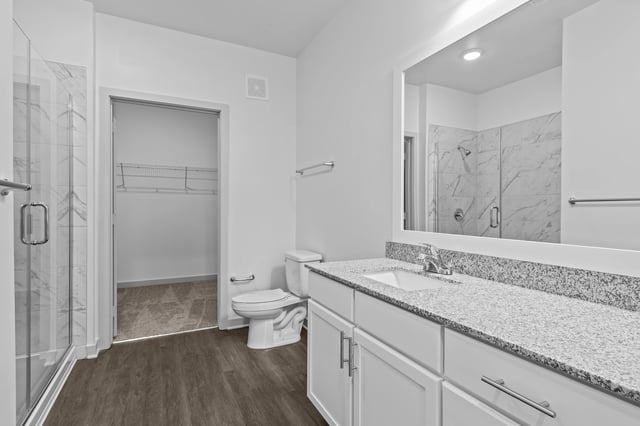 Modern bathroom with a granite countertop, white vanity, toilet, and walk-in shower.