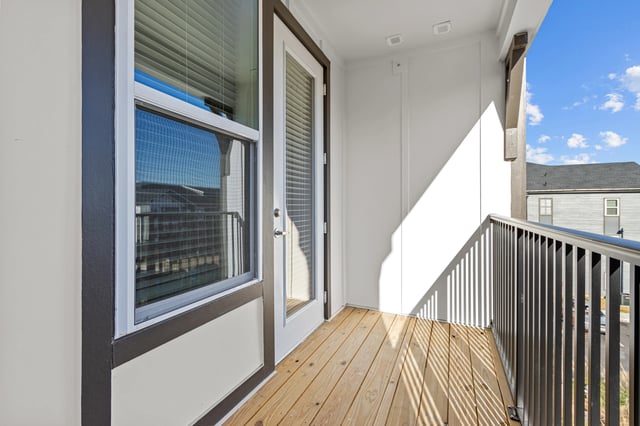 Balcony with wooden floor and metal railing, overlooking buildings.