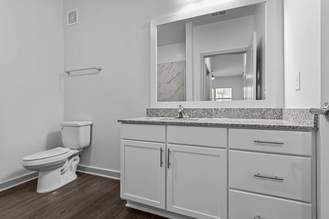 Modern bathroom vanity with granite countertop, sink, large mirror, and toilet.