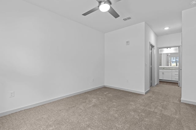 Empty bedroom with neutral carpet and a ceiling fan, leading to a bathroom.