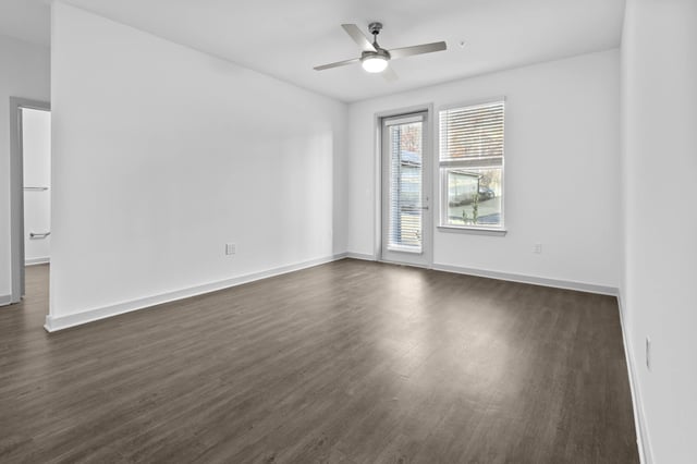 Spacious empty living room with a ceiling fan, wood-look flooring, and a door to a patio.
