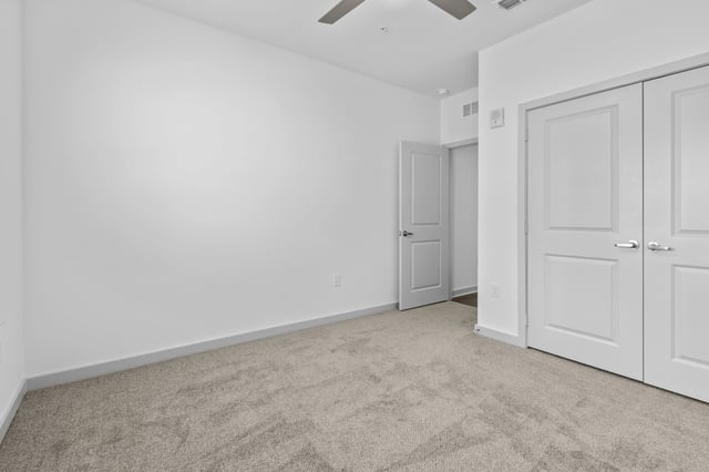 Empty room with neutral carpet and white walls, showing a ceiling fan and two doors.