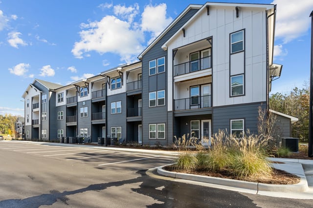 Modern apartment building exterior with balconies and parking lot.