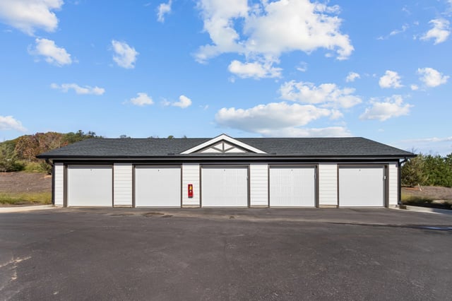 Row of six white garage doors on a white building with a dark roof.