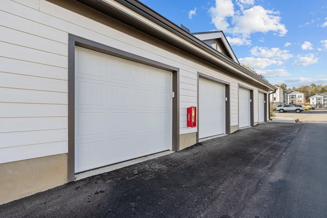 Row of garages with white doors and a red fire extinguisher box mounted on the wall.