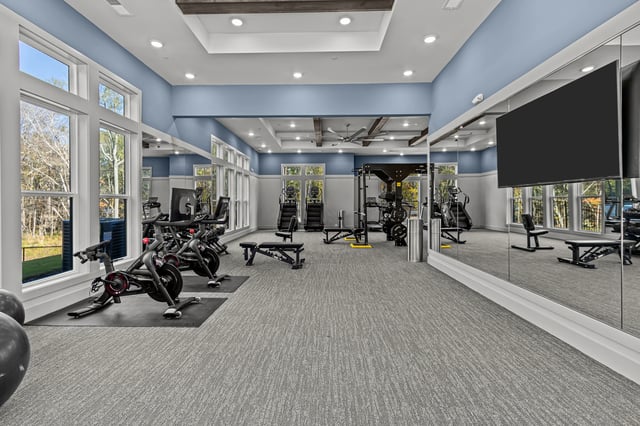 Gym equipment including stationary bikes, treadmills, and weight machines, with large mirrors and bright lighting.