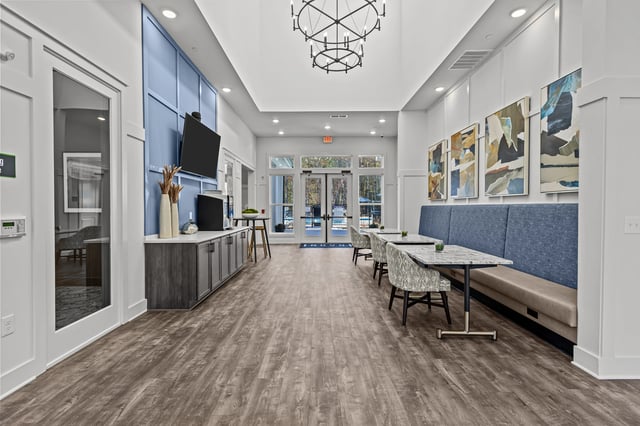 Interior of a modern apartment building lobby with a seating area, tables, and a view of the pool through the doors.