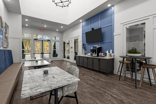 Community lounge area with marble-top tables, comfortable seating, and a coffee station.
