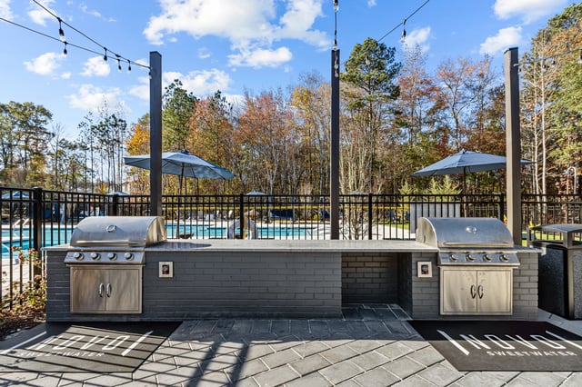 Outdoor kitchen area with two grills and a pool in the background.