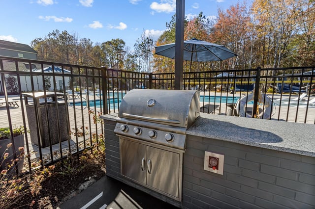Outdoor grill with a built-in kitchen counter and seating area, next to a swimming pool.